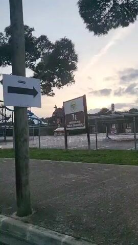 The video pans across a closed waterpark, with a large waterslide structure visible behind a fence.  The sky is a pale twilight.  There are a few trees and a crosswalk. The video is shot from a low angle, seemingly from a moving car.  A parking sign is visible at one point.  The area appears deserted.