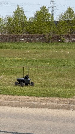Black robot with antennas crosses grassy field in Riga