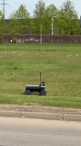 Black robot with antennas crosses grassy field in Riga