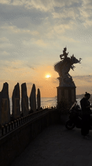 Sunset gathering at Indonesian beach features mythological statues, kite flying