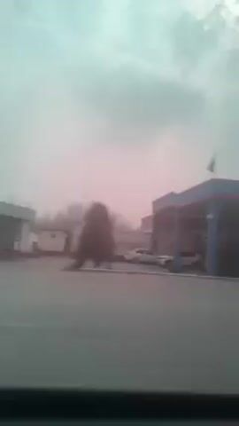 A car is driving down a road, passing a gas station and a few buildings. The sky is overcast and the light is a little hazy.