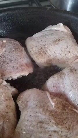 The image shows chicken pieces being fried in a pan. Four pieces of seasoned raw chicken are visible, with visible flecks of black pepper. The chicken is in a dark, non-stick pan, with a small amount of oil or rendered fat visible. The scene appears to be a kitchen environment, possibly during a meal preparation. There is no visible text. The lighting suggests it is daytime, but no specific time can be determined. No people are visible in the frame. The image's focus is on the food being cooked, creating a sense of domestic activity. The location context of Horenka, Ukraine, is noted, but no specific visual cues within the image confirm this location.