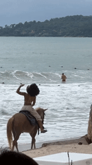 Woman rides horse into ocean waves at beach