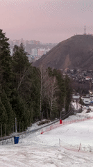 Snowboarder captures first-person descent down snowy slope near city