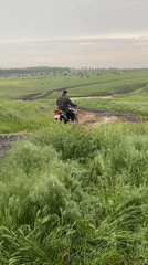 Motorcyclist gets stuck in muddy field during overcast conditions