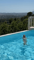Two women swim in infinity pool overlooking forested mountains