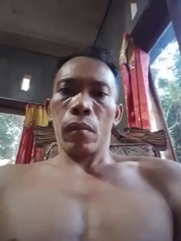 A close-up shot shows a bare-chested man looking directly at the camera. The man has short, dark hair and appears to be indoors, possibly in a room with a window. The background is blurred but suggests a rustic setting with curtains and wooden elements. The lighting is dim, casting shadows on the man's face and chest. The man's expression is neutral. The timestamp indicates the video is 4 seconds long.