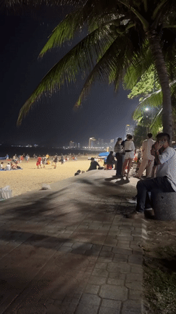 Crowded beachfront promenade at night near an LED-lit venue
