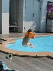 Child jumps into swimming pool wearing orange floaties