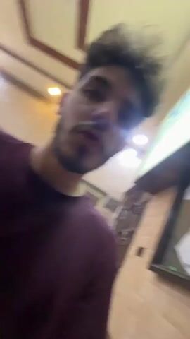 The video shows a man in a maroon shirt walking towards an elevator. The elevator is modern with a mirrored interior and a digital floor display showing "0". The man presses the call button, the elevator door opens, and he enters the elevator. The video ends with him inside the elevator.