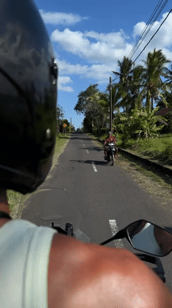 Motorcycle rider travels past two men on Indonesian road