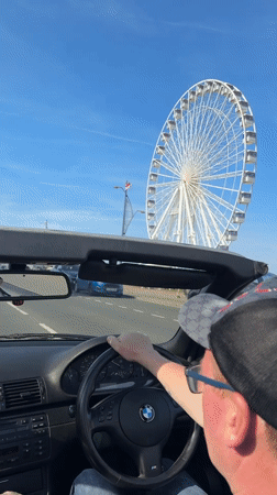 Convertible driver passes Great Yarmouth Ferris wheel on sunny day