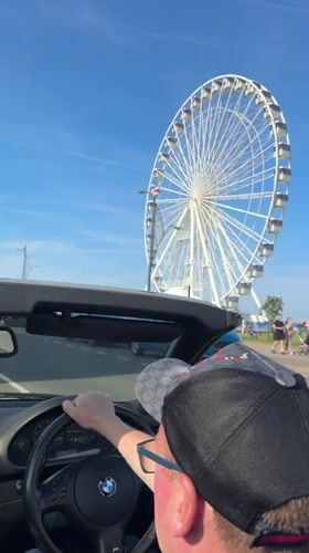 Convertible driver passes Great Yarmouth Ferris wheel on sunny day