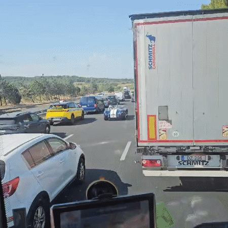 Blue convertible with racing stripes cruises French highway traffic