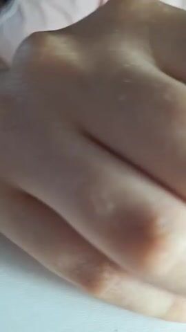 This media file features a close-up view of a person's hands and fingernails. The subject appears to be in the process of having their nails done, likely a manicure or artificial nail application.

The hands are fair-skinned and show several fingers with long, square-shaped artificial nails. These nails are a pale, translucent yellowish-green color, giving them a somewhat milky appearance. The cuticle area of the natural nail is visible beneath the artificial tips.

In the background, out of focus, elements of a workspace can be discerned. To the left, a grey object with a rounded dome shape, possibly a UV or LED lamp used for curing nail polish or gel, is visible. A person's arm and torso, wearing a light pink garment, are also partially visible. The lighting suggests an indoor setting, possibly during the daytime due to the brightness.

The overall mood conveyed is one of focus and meticulous activity, typical of a beauty or personal care treatment. There is no visible text in the media file. The location context of Drepcăuți, Moldova, indicates the general geographical area where this scene is taking place.