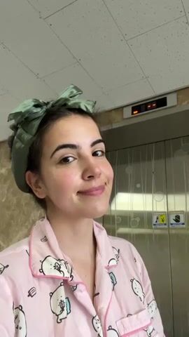A woman in pink pajamas with a cartoon print and a green headband stands in an elevator and waves. The elevator doors open on the tenth floor. She pans the camera to show the number ten on the wall, a water cooler, and a door.