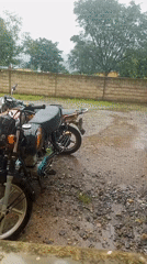 Motorcycles parked on wet gravel lot in rainy Serti