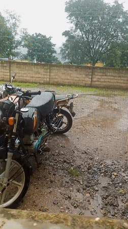 Motorcycles parked on wet gravel lot in rainy Serti