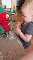 Toddler shares snacks with pepper plush toy on couch