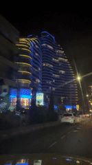 Nighttime street view past a wavy-facade skyscraper in Cyprus