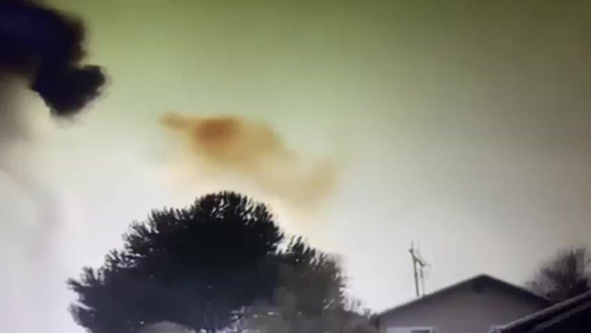 A white car is parked in a driveway. The car is facing away from the viewer. There is a mailbox to the right of the car. There are trees and grass surrounding the driveway. The scene appears to be at night. The footage is grainy and out of focus in some areas.