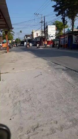 The video begins with a wide shot of a street. A person is walking down the street, and there is a motorcycle in the distance. The street is lined with buildings, and there are trees on the side of the road. The sky is blue, and the sun is shining. The video then zooms in on a building, and the person is walking past it. There is a sign on the building that says "ITL-IEX." The video then zooms out, and the person is walking down the street again. There is a motorcycle in the distance. The video then ends with a shot of the street.