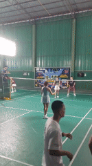 Indoor badminton doubles match observed with referee present