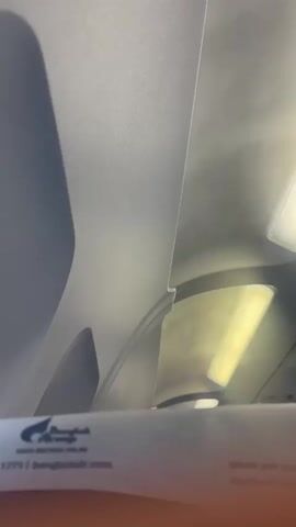 The video shows a close-up view of the interior of an airplane cabin, looking upwards towards the ceiling. A portion of a paper magazine or information booklet is visible in the foreground, with a logo that appears to be for Bangkok Airways. Above the booklet, the curved ceiling panels of the airplane are visible, with a soft, yellowish light emanating from an overhead light fixture. The lighting creates shadows and highlights on the ceiling, suggesting a low-light environment typical of an airplane cabin. The overall impression is one of a serene and enclosed space.
