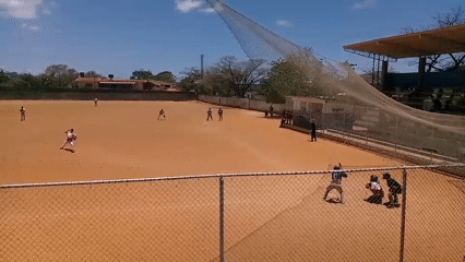 Baseball game played on sunny afternoon, witnessed through fence