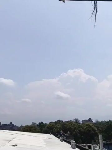 The video shows a clothesline with a striped towel hanging on it. The sky is blue with some white clouds. In the background, there are buildings and trees. The camera pans slightly to the left and then to the right.