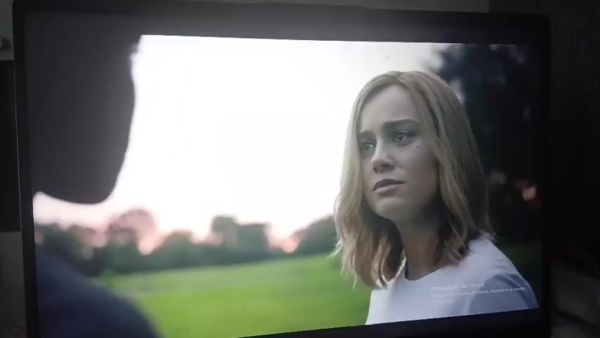 This media file captures a scene from a movie or TV show, likely taking place outdoors during daylight. The primary subjects are two women, both in close-up shots. The first woman, with blonde, shoulder-length hair and a white t-shirt, appears concerned or thoughtful. The second woman, with short, dark, layered hair and a denim jacket over a red top, has a more serious expression. She is also wearing a necklace with a gold pendant.

The scene is set against a backdrop of greenery, suggesting a park or field, with trees visible in the distance. The lighting indicates it might be late afternoon or early evening, with a bright, overcast sky.

The interaction between the two women appears to be a conversation or a moment of emotional exchange, given their direct gazes and facial expressions. One shot shows the blonde woman looking directly at the camera, while another shows her with a slight smile, looking away. The darker-haired woman is looking towards the blonde woman.

A small text overlay is visible in the bottom right corner of the screen, which reads "Активация Windows. Чтобы активировать Windows, перейдите в раздел 'Параметры'". This translates to "Windows Activation. To activate Windows, go to 'Settings'". This is likely a watermark from the operating system on which the media is being displayed.

No specific location cues within Nizhneangarsk, Russia are evident. The activity is the unfolding of a dramatic or emotional scene between the two characters.
