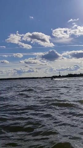 A person is riding a jet ski on a body of water. The sky is blue with white clouds. The water is choppy.