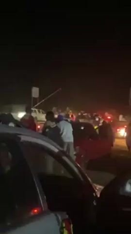 The video shows a nighttime scene with a large crowd of people and numerous cars. It appears to be a New Year's celebration. People are milling around and standing near or on top of cars. The lighting is poor, making details difficult to discern. There are visible headlights and taillights from the vehicles. The person recording the video says "Happy New Year, guys. Happy New Year."