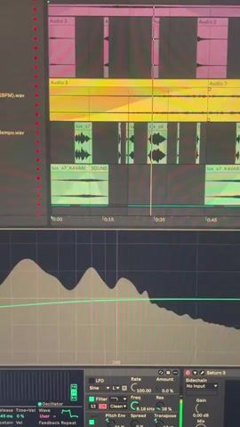 The video shows a close-up of a computer screen displaying a music production software interface. The upper part of the screen exhibits a timeline with several audio tracks in various colors like pink, yellow, and green. Audio clips are arranged sequentially within these tracks. A vertical line is visible around the 0:30 mark, potentially indicating the current playback position. The lower part of the screen showcases a waveform display along with parameter controls for effects or synthesizers. Parameters such as "LFO", "Rate", "Freq", "Res", "Pitch Env", and "Transpose" are adjustable. A plugin named "Saturn 2" is mentioned on the right, suggesting the software is being used for sound design or mixing purposes. The overall setting indicates someone is likely working on music production or audio editing.