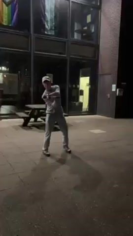 Here's a description of the video:

The video shows a man outdoors at night. He's wearing a baseball cap, a light-colored sweatshirt, and jeans. He appears to be throwing a rock or a small object toward a building that says "Grizedale College" in white lettering with a wild boar logo above the text. The building is dark, with lit windows visible in the background. There's a picnic table near him. After the man throws the object, the camera pans to the left, focusing on the building's facade.