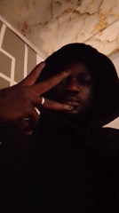 Person in hoodie makes peace signs, covers face indoors