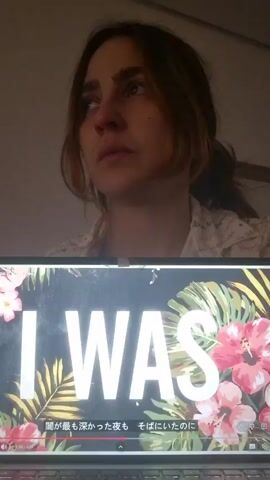 A woman is shown in the top portion of the video, drinking from a white mug while watching a music video on a laptop. The music video shows tropical flowers and ferns on a black background. White text appears in the center of the video, starting with the word "THERE" then "YOU" then "IN YOUR DARK" then "BUT" then "WHERE." Subtitles are displayed in Japanese.