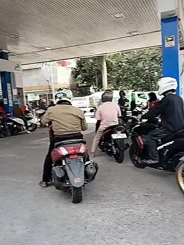 The video shows a gas station with several motorcycles lined up. People are waiting on their motorcycles, presumably to refuel. The overall scene is consistent with a busy gas station. The time stamp indicates the video lasts for four seconds.