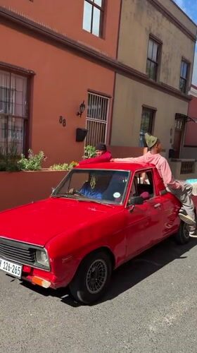 Red pickup with three men drives Cape Town street
