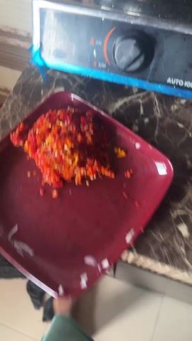 The video shows someone cooking in a kitchen. Initially, the camera focuses on a stove with a pot on it. Inside the pot, sliced onions are being sauteed with oil. The camera then shifts to a cutting board with diced tomatoes and peppers, accompanied by a large kitchen knife. A blender is visible in the background.