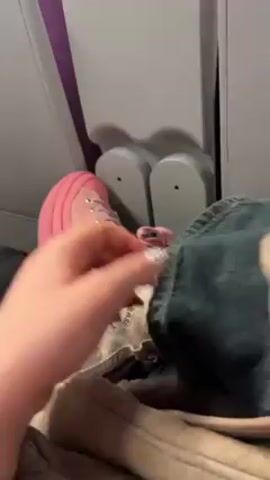 Here is a description of the video.

The video shows a person on an airplane. They are wearing pink and white Converse high-top sneakers and pink socks with a heart pattern. The person is also wearing denim jeans. The airplane seat is beige. The person’s hand, which is wearing rings and has painted nails, is visible near their leg. The airplane window shade is up.