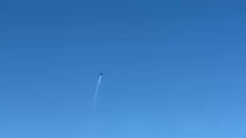 A small aircraft is seen performing a vertical climb against a clear blue sky, leaving a white contrail behind it. The aircraft stalls or performs a maneuver at the top of its climb, causing it to curve slightly before beginning its descent.