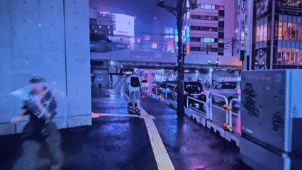 Nighttime rainfall creates reflective street scene with umbrella-carrying pedestrians