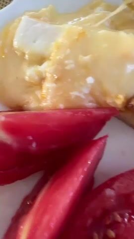 The video shows a close-up of a meal served on a white plate. The meal appears to consist of a savory pastry or quiche, possibly with cheese, and sliced tomatoes. A fork is visible in the upper right corner, interacting with the pastry. The tomatoes are bright red and appear to be fresh. The lighting is natural and bright, suggesting an indoor setting, possibly a kitchen or dining area. There are no people visible in the video.