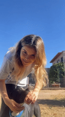 Woman pets dog, takes selfie in sunny Sumalao yard