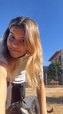 Woman pets dog, takes selfie in sunny Sumalao yard