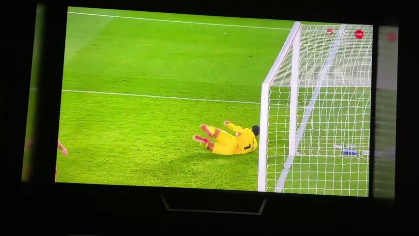 The video shows a TV screen displaying a soccer match between BAR and ATM. The score is 0-2. The time on the screen is 78:45. A man in a green uniform is holding up a sign that has the HUBLOT logo on it. Two players, wearing the numbers 23 and 11, are standing next to him. A bald man in a dark suit stands to the left of the man in green. The stadium is filled with people.