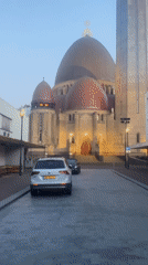 White SUV parked on cobblestones near a domed building in Waalwijk