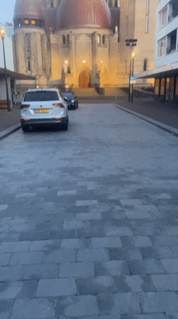 White SUV parked on cobblestones near a domed building in Waalwijk