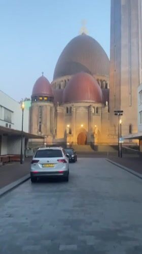 White SUV parked on cobblestones near a domed building in Waalwijk